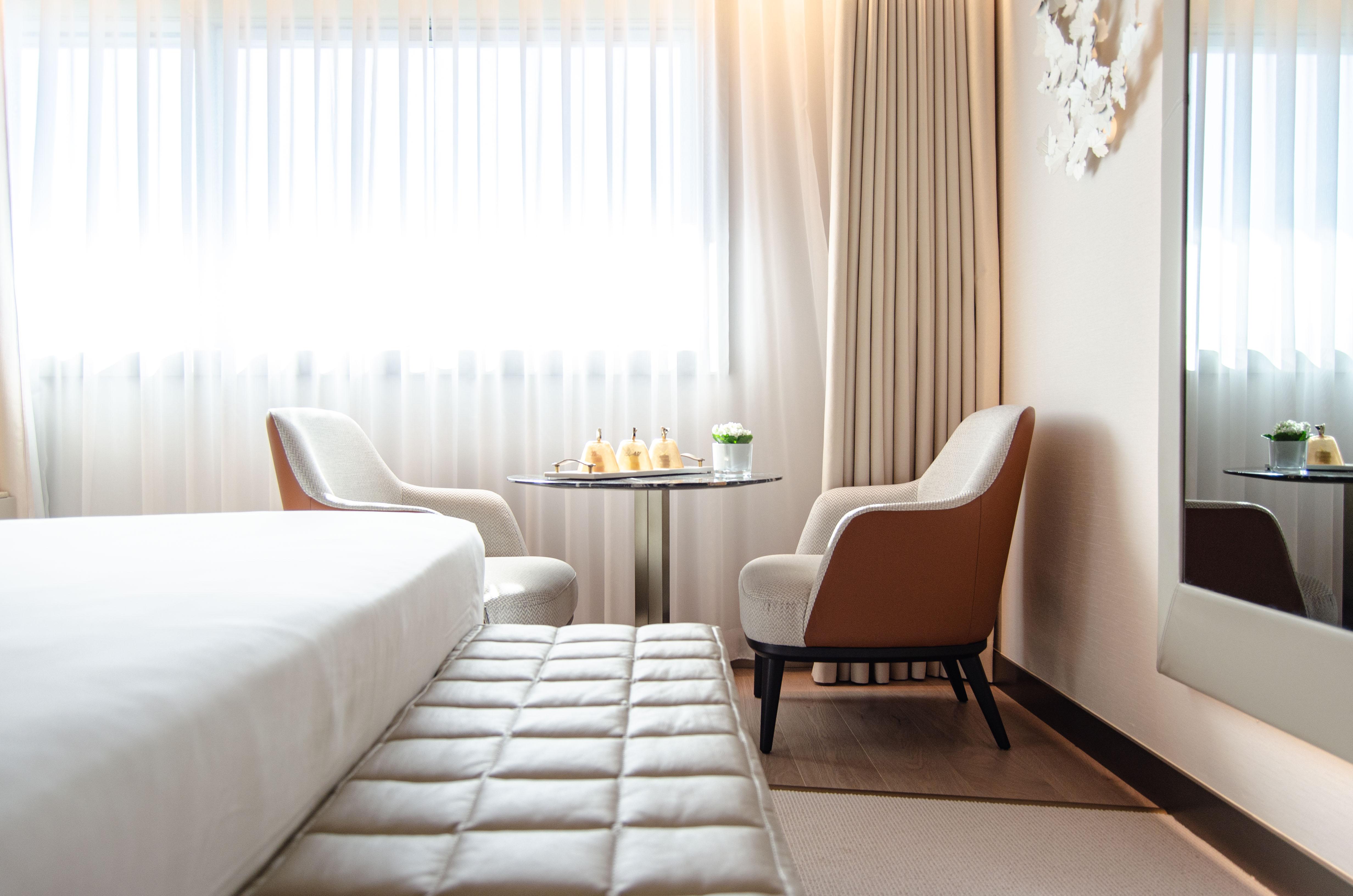 ליסבון Epic Sana Marques Hotel מראה חיצוני תמונה The photo shows a modern, well-lit hotel room featuring a bed with a minimalistic design. To the side, there are two stylish chairs positioned around a small, round table. On the table, there are some bottles and a glass, possibly indicating refreshm