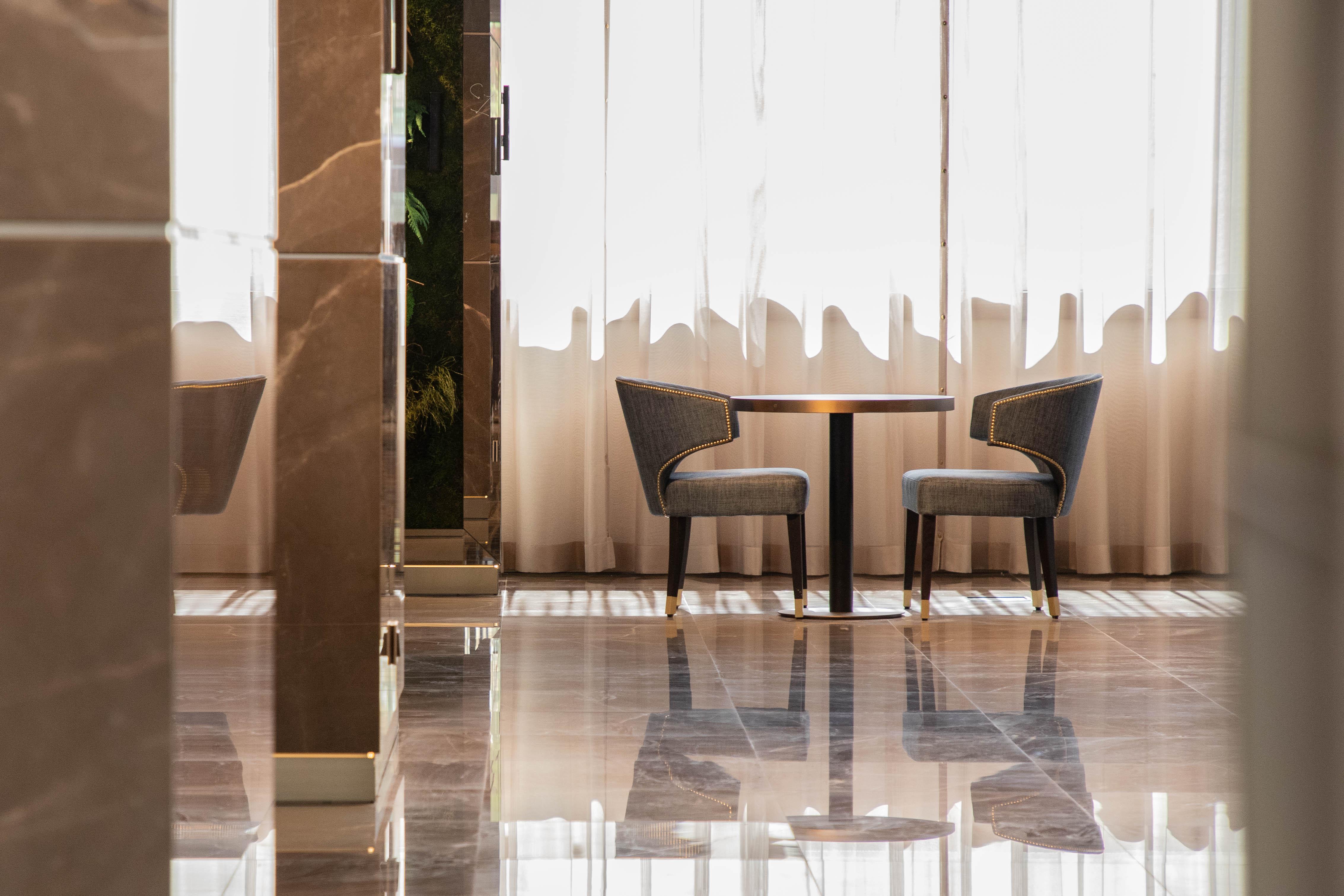 ליסבון Epic Sana Marques Hotel מראה חיצוני תמונה The photo shows a modern, elegant interior space featuring a small round table accompanied by two upholstered chairs. The setting is well-lit with natural light streaming in through large, sheer curtains, creating a warm and inviting atmosphere. The 