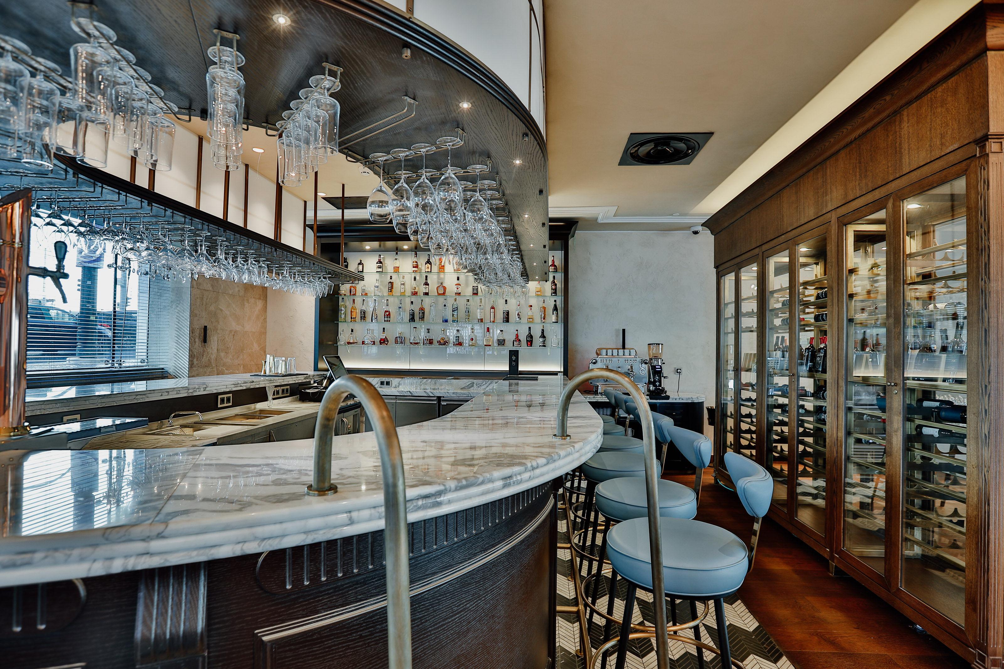 ליסבון Epic Sana Marques Hotel מראה חיצוני תמונה The photo depicts a stylish bar area. There is a curved bar counter made of marble, which features elegant glassware hanging overhead. The bar is well-lit, showcasing a selection of bottles on the shelves behind it. There are several blue upholstered