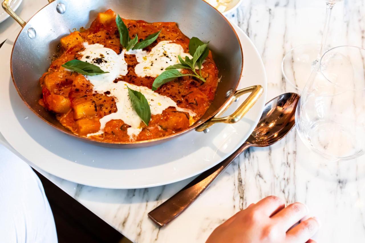 ליסבון Epic Sana Marques Hotel מראה חיצוני תמונה The photo shows a dish of gnocchi served in a creamy tomato sauce. The gnocchi pieces are orange and appear to be mixed with herbs, while there are dollops of a white creamy sauce on top. Fresh basil leaves are scattered on the dish for garnish. The 