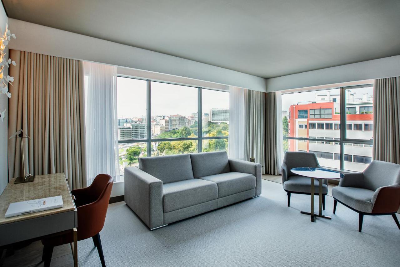 ליסבון Epic Sana Marques Hotel מראה חיצוני תמונה The photo shows a modern hotel room featuring a light, airy atmosphere. There is a large window with sheer curtains that allows natural light to flood the space, offering a view of the cityscape outside. Inside, the room includes a comfortable sofa i