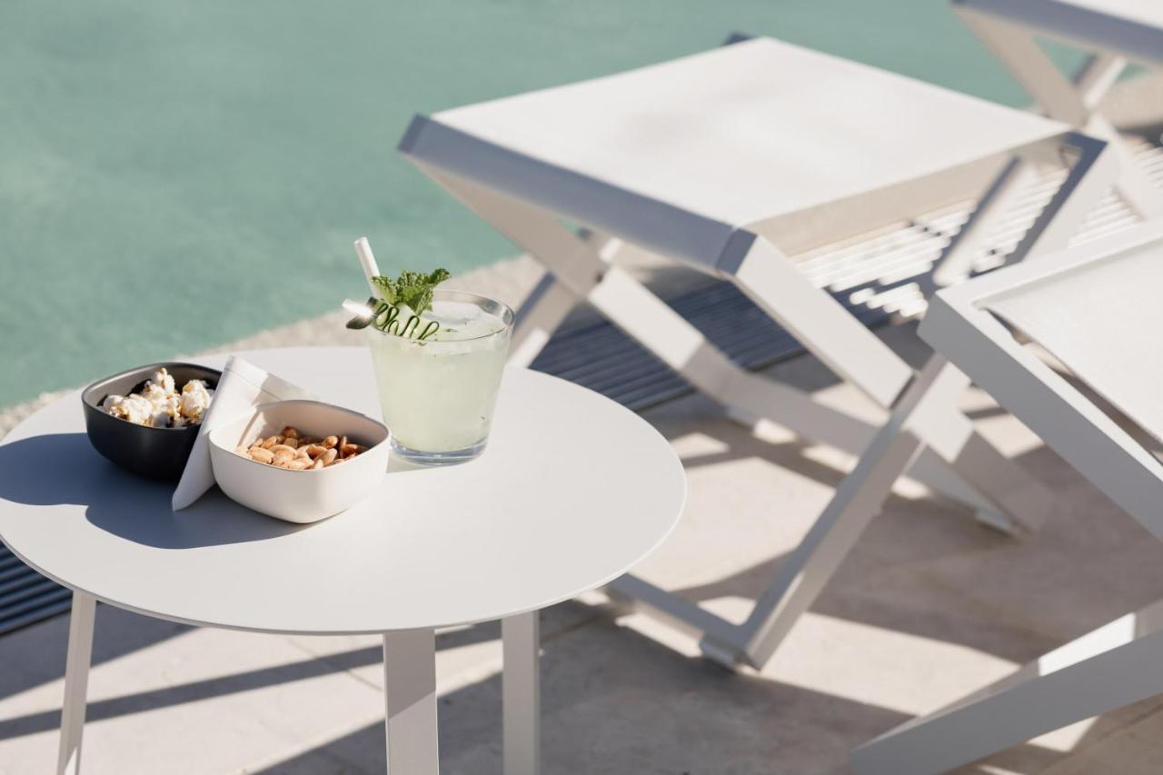 ליסבון Epic Sana Marques Hotel מראה חיצוני תמונה The photo shows a light, modern setting by a pool. In the foreground, there's a small round table with two bowls of snacks: one has popcorn, and the other contains mixed nuts. Beside the bowls, there’s a refreshing cocktail in a glass, garnished with