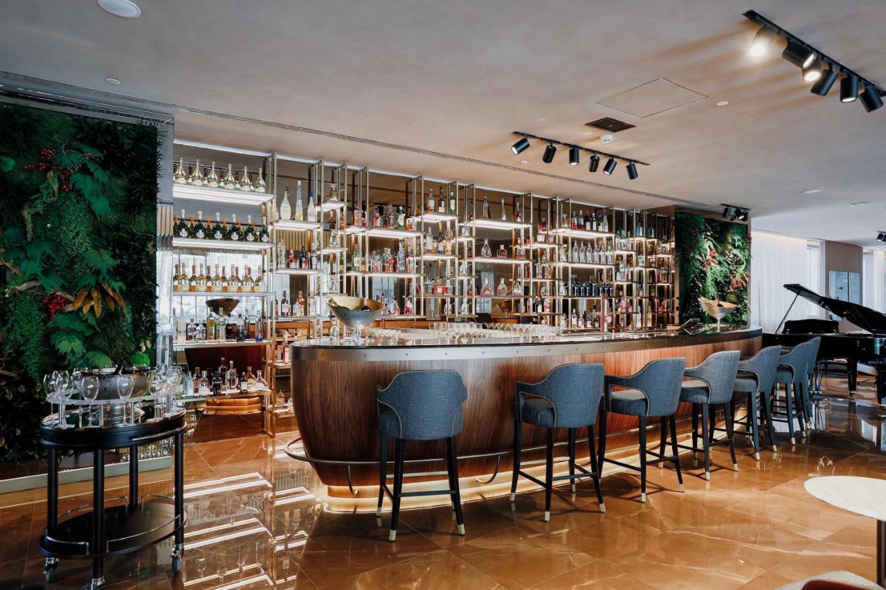 ליסבון Epic Sana Marques Hotel מראה חיצוני תמונה The photo shows a modern bar interior. In the foreground, there is a sleek, curved bar with a shiny surface. Behind the bar, a well-organized shelf displays a wide variety of bottles, illuminated by ambient lighting. The bar stools are upholstered in
